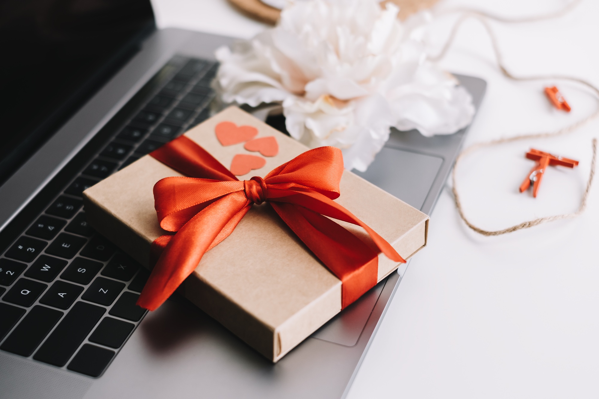 Gift box with red ribbon and hearts on the table near laptop. Valentine's day surprise concept
